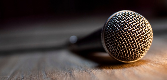 Close-up of a professional microphone resting on a wooden surface, with focus on the mesh grille, ideal for podcasting, public speaking, or audio recording visuals.
