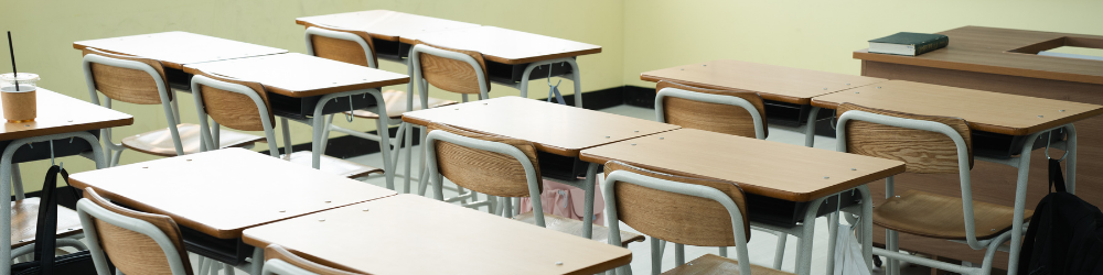 Empty classroom at High School with wooden desks, chairs, and teacher’s desk with no students present.