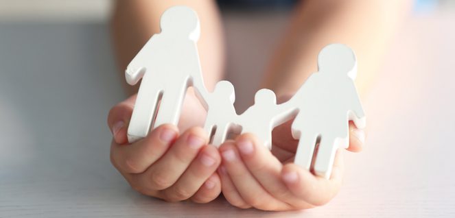 Hands holding paper cut-out figures of a family, two adults and two children, symbolizing family unity, legal support, and protection services, with a softly blurred background.
