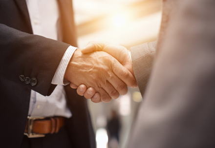 Two professionals in formal business attire shake hands in a warmly lit setting, symbolizing trust, agreement, or the successful completion of a deal.